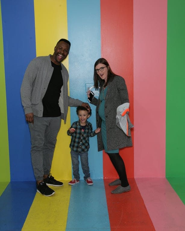 A man, woman, and child standing in front of a multi - colored wall