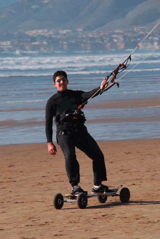 A man riding a skateboard while holding a kite on top of a sandy beach