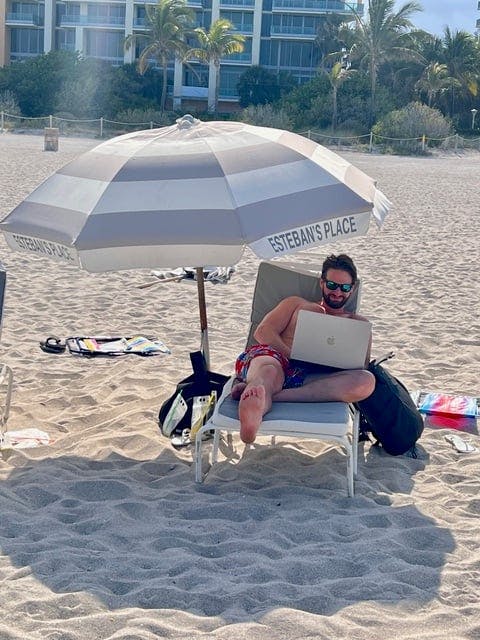 A man sitting in a chair on a beach using a laptop