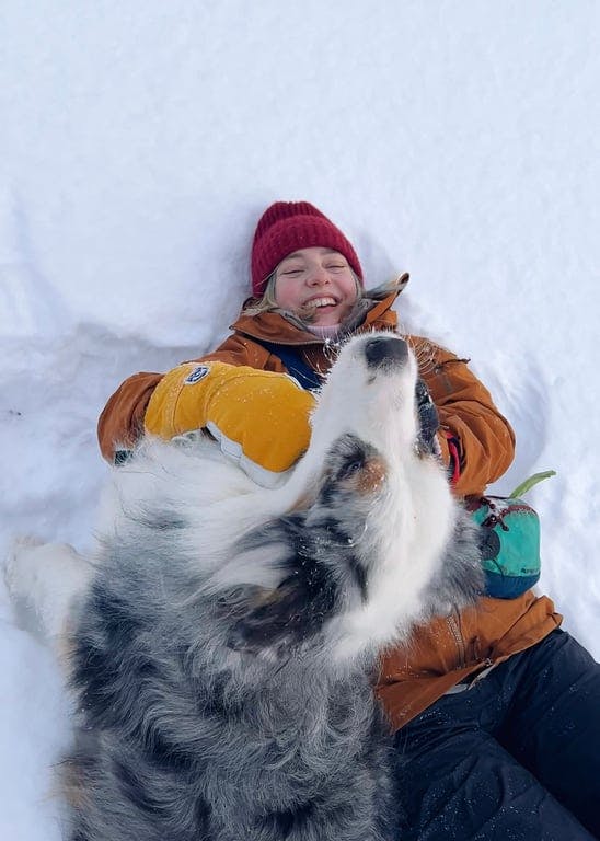 A person laying in the snow with a dog