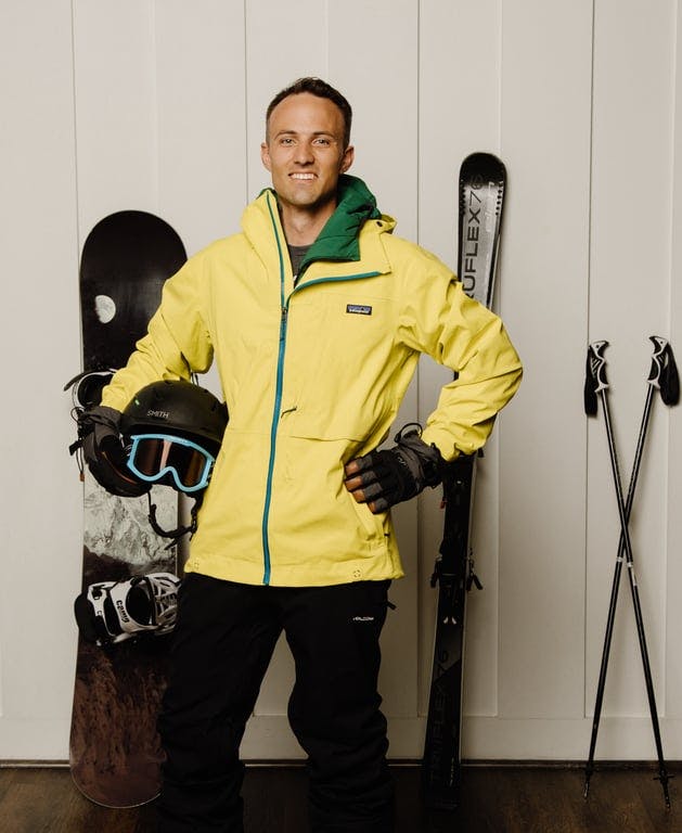 A man in a yellow jacket standing next to a snowboard